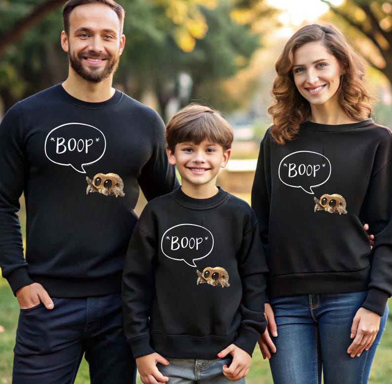 Puede incluir: Sudaderas negras con un dibujo de ara&ntilde;a de dibujos animados y la palabra "BOOP" en una burbuja de di&aacute;logo. La imagen muestra a una familia con sudaderas a juego, ideal para una salida familiar o un evento tem&aacute;tico.
