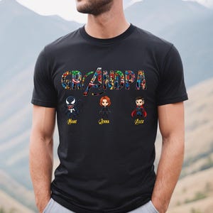 Peut inclure: Un t-shirt noir &agrave; manches courtes avec le mot GRANDPA &eacute;crit dans une police compos&eacute;e d'un collage de personnages de bandes dessin&eacute;es. Sous le texte se trouvent trois figurines de style chibi de Venom, Black Widow et Doctor Strange.