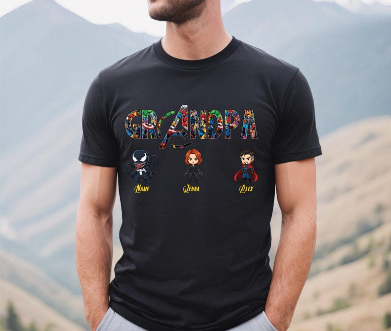 Peut inclure: Un t-shirt noir &agrave; manches courtes avec le mot GRANDPA &eacute;crit dans une police compos&eacute;e d'un collage de personnages de bandes dessin&eacute;es. Sous le texte se trouvent trois figurines de style chibi de Venom, Black Widow et Doctor Strange.