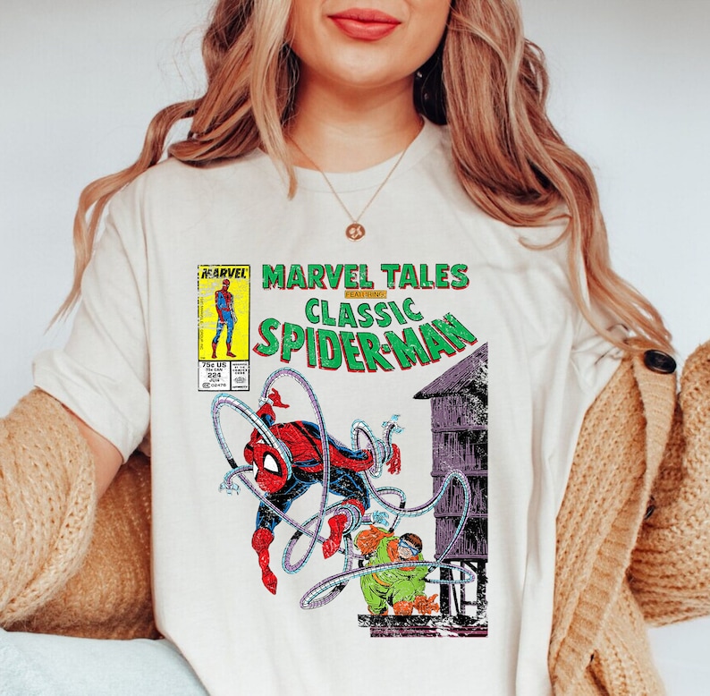 May include: Cream-colored t-shirt featuring a Marvel Tales Classic Spider-Man comic book cover design. The graphic includes Spider-Man in a red and black suit, along with the text "MARVEL TALES CLASSIC SPIDER-MAN".