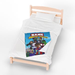 May include: A child's bed with a white comforter and pillow. A colorful blanket featuring cartoon superheroes and the text "NAME AMAZING FRIENDS" is draped over the bed. The bed frame is made of light-colored wood.