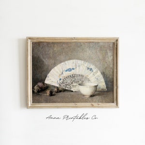 May include: A framed print of a still life featuring a white and blue fan, a white bowl, and pine cones on a brown background.