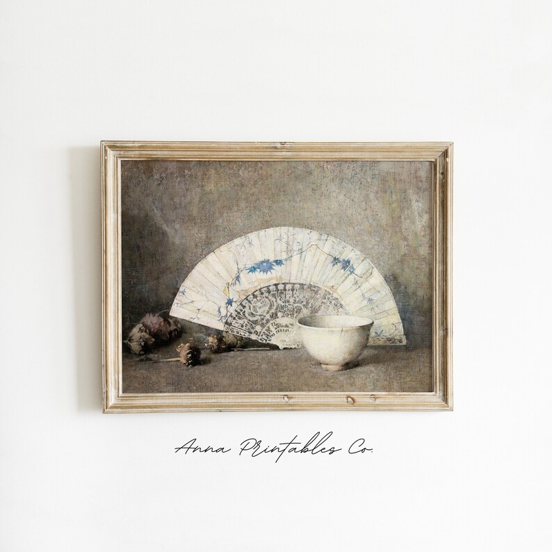 May include: A framed print of a still life featuring a white and blue fan, a white bowl, and pine cones on a brown background.