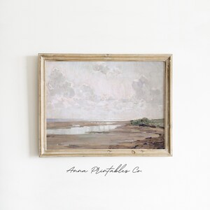 May include: A framed painting of a seascape with a light blue sky and white clouds. The painting depicts a beach with a calm body of water and a small patch of green vegetation in the foreground.