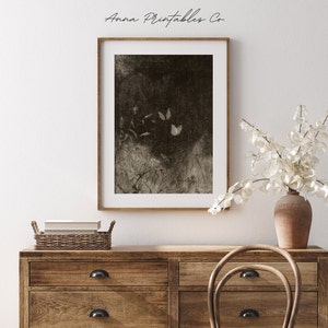 May include: A sepia-toned framed print featuring a dark, textured background with three butterflies and delicate plant life. The print is displayed above a wooden dresser with a woven basket and a vase of white flowers.