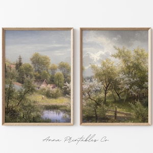 Pode incluir: Duas pinturas de paisagem emolduradas que retratam uma cena rural com árvores, um lago e uma pequena casa. As pinturas estão em uma moldura de madeira clara e estão penduradas em uma parede branca.