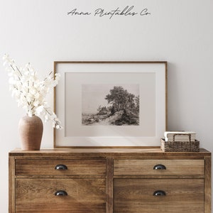 May include: A black and white photograph of a landscape with a large tree in the foreground. The photograph is framed in a wooden frame and is displayed on a wooden dresser with two drawers.