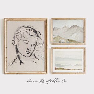 May include: Three framed art prints on a white wall. The left print is a black and white line drawing of a person's face. The middle print is a watercolor painting of a mountain range. The right print is a watercolor painting of a seascape.