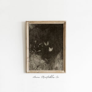 May include: Sepia-toned framed print featuring a field with butterflies. The artwork has a vintage aesthetic, with a dark background and delicate details of plants and insects. The frame is a light, neutral color, and the text "Anna Printables Co." is at the bottom.