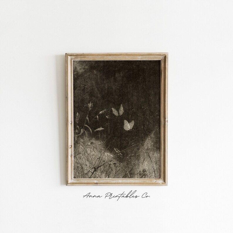 May include: Sepia-toned framed print featuring a field with butterflies. The artwork has a vintage aesthetic, with a dark background and delicate details of plants and insects. The frame is a light, neutral color, and the text "Anna Printables Co." is at the bottom.
