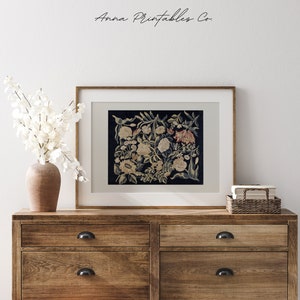 May include: A framed print of a vintage floral tapestry with a dark blue background and white, yellow, and red flowers. The print is in a wooden frame and is hanging on a white wall.