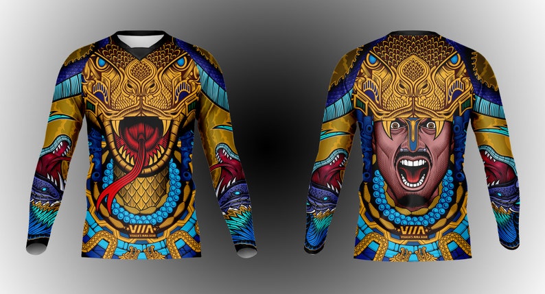 May include: A long-sleeved shirt with a colorful design featuring a golden snake head with a red tongue and a warrior's face with a blue and gold background. The shirt has the text "VIIA" on the bottom.