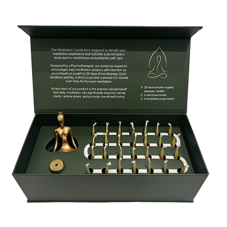 May include: A green box with a gold meditating figure and 28 small yellow beeswax candles. The box is open and the candles are arranged in a grid. The text on the box reads: "The Meditation Candle kit is designed to elevate your meditation experience and cultivate a sacred space dedicated to mindfulness and authentic self-care."