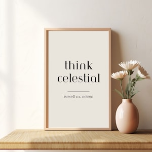 May include: A framed print with the text "think celestial" and the name "russell m. nelson" underneath. The print is on a wooden shelf with a vase of white flowers to the right.