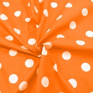 May include: Close-up of orange fabric with a pattern of large, white polka dots. The fabric is gathered and folded, creating shadows and texture. The polka dots vary in size and are evenly spaced across the material.