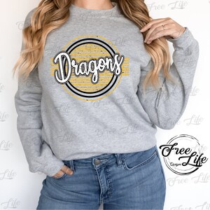 K&ouml;nnte beinhalten: Ein graues Sweatshirt mit einem gelben und schwarzen Kreisdesign, auf dem in einer Retro-Schrift "Dragons" steht.