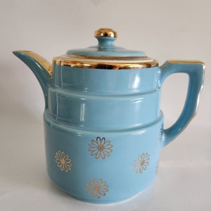 May include: A light blue ceramic teapot with a gold trim and a floral design. The teapot has a lid and a handle.