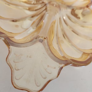 May include: A clear glass dish with a scalloped edge and a swirl design. The dish is a light amber colour and has a shiny finish.