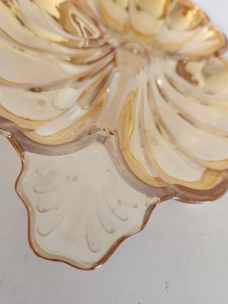 May include: A clear glass dish with a scalloped edge and a swirl design. The dish is a light amber colour and has a shiny finish.