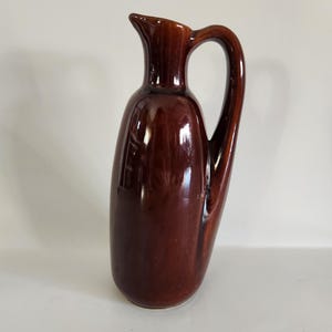 May include: A brown ceramic pitcher with a rounded body and a handle. The pitcher has a glossy finish.