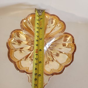 May include: A clear glass dish shaped like a four-leaf clover with a gold iridescent finish. The dish is approximately 15 cm wide.