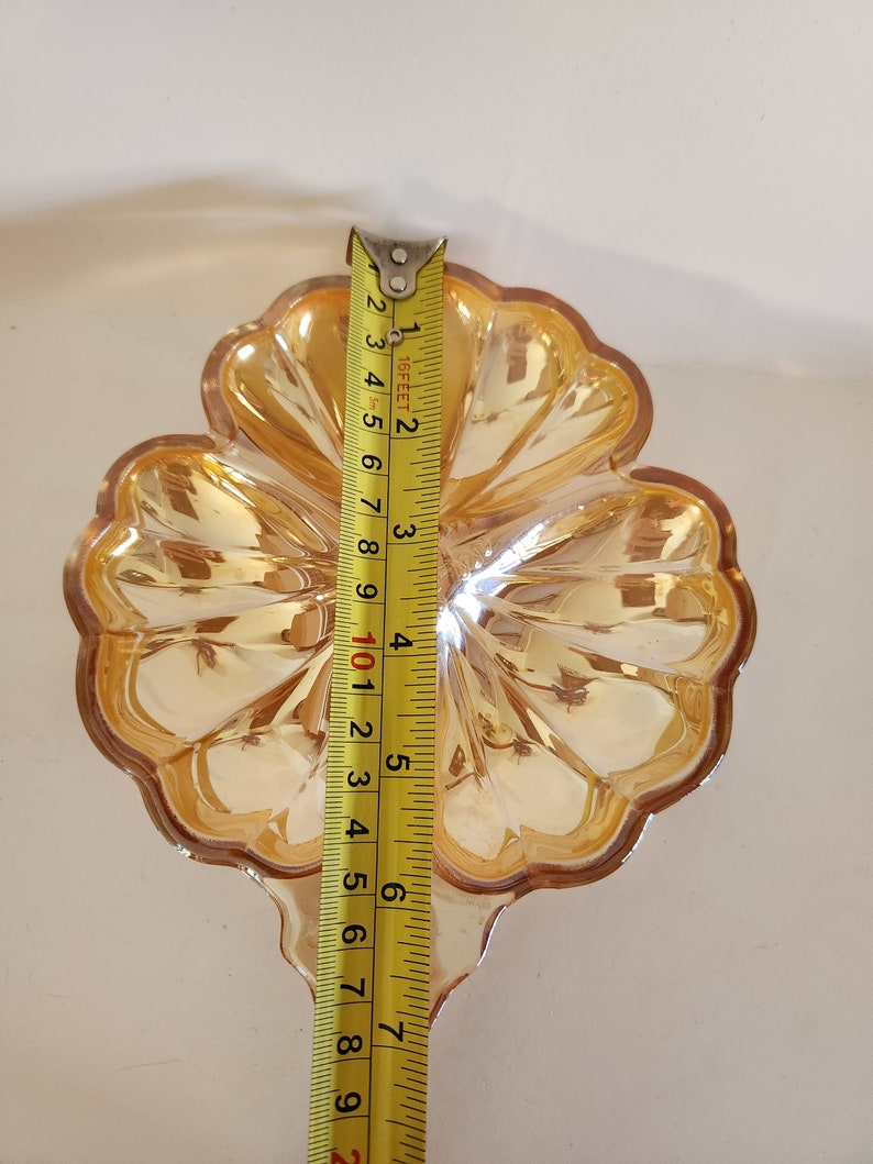 May include: A clear glass dish shaped like a four-leaf clover with a gold iridescent finish. The dish is approximately 15 cm wide.