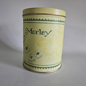 May include: A yellow metal canister with a green and white floral design and the word "Morley" printed on the front.