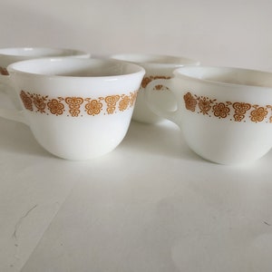 May include: Set of four white ceramic coffee mugs with a brown floral pattern around the rim.
