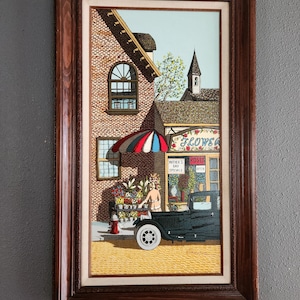 May include: Framed painting depicting a flower shop scene. The artwork features a brick building with a flower shop, a black vintage car, and a woman arranging flowers. The shop has a striped umbrella and the text "Mother's Day Specials".