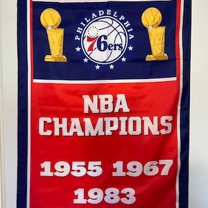 May include: A red and blue banner with the Philadelphia 76ers logo and the text "NBA CHAMPIONS 1955 1967 1983". The banner has stars on the top and bottom.