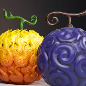 Könnte beinhalten: Zwei detaillierte, kugelförmige Früchte mit Fantasy-Thema. Eine ist gelb, orange und rot mit einem grünen Stiel. Die andere ist tiefblau mit einem braunen Stiel. Beide haben komplizierte, wirbelnde Muster.