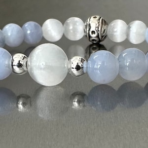 May include: A bracelet made with light blue and white beads with a silver charm in the center.