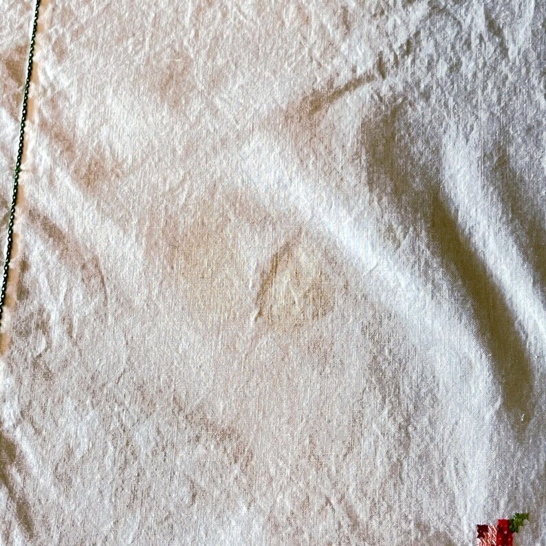 May include: Close-up of a white, textured fabric with subtle brown stains. A thin green chain runs along the left edge. The fabric is slightly crumpled, with visible folds and shadows.