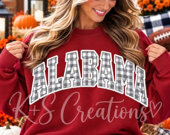 May include: A maroon crewneck sweatshirt featuring the word ALABAMA in a white-outlined, grey and white buffalo plaid pattern across the chest. The garment has long sleeves and a ribbed neckline, providing a classic fit for casual wear.
