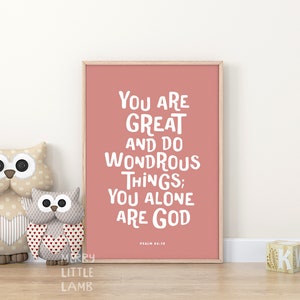 Könnte beinhalten: Ein rosa gerahmter Druck mit dem Text "You are great and do wondrous things; You alone are God" in weißen Buchstaben. Der Text stammt aus Psalm 86:10. Der Druck befindet sich an einer weißen Wand mit zwei Eulen-Plüschtieren davor.