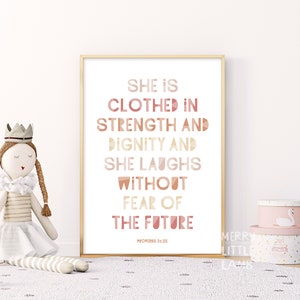 Può includere: Una stampa incorniciata con un design sfumato rosa e pesca. Il testo recita "Lei è vestita di forza e dignità e ride senza paura del futuro. Proverbi 31:25".