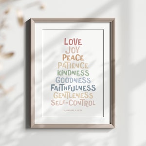 May include: A framed print with a white background and a rainbow-colored list of words: Love, Joy, Peace, Patience, Kindness, Goodness, Faithfulness, Gentleness, Self-Control. The words are arranged in a pyramid shape. The text "Galatians 5:22-23" is printed in small letters at the bottom of the print.