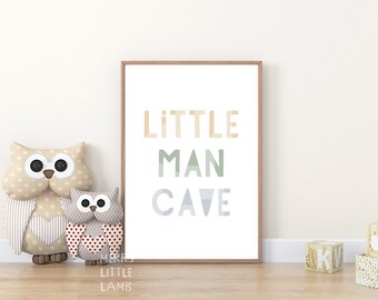 May include: A framed print with the text "LITTLE MAN CAVE" in a colorful, layered font. The print is displayed on a light wood floor with two owl stuffed toys in front of it.