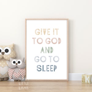 May include: A framed print with the text "Give it to God and go to sleep" in a colourful, geometric font. The print is displayed on a white wall with two owl stuffed toys in front of it.