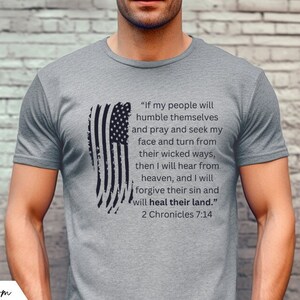 Pode incluir: Uma camiseta cinza mescla com um gráfico de bandeira americana em preto e branco e uma citação de 2 Crônicas 7:14. A citação diz: "Se o meu povo se humilhar e orar e buscar a minha face e se afastar dos seus caminhos perversos, então eu ouvirei dos céus, e eu perdoarei o seu pecado e curarei a sua terra."