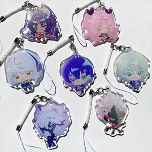 Op de afbeelding: Zeven acryl bedels met anime-stijl personages in verschillende kleuren. Elke bedel heeft een uniek ontwerp en is bevestigd aan een wit koord met een zilveren sluiting. De personages hebben gedetailleerde gezichtskenmerken en kleurrijke outfits.