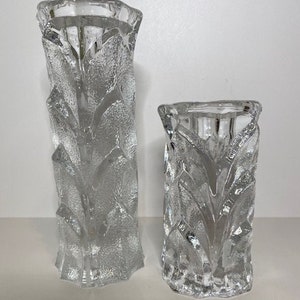 May include: Two clear glass vases with a textured leaf design. The vases are different sizes, with the taller vase being about 10 inches tall and the shorter vase being about 6 inches tall.