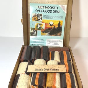 May include: Open cardboard box containing a latch hook rug kit. The kit includes bundles of yarn in various colors, a ruler, and a printed instruction sheet with the text "GET HOOKED ON A GOOD DEAL."