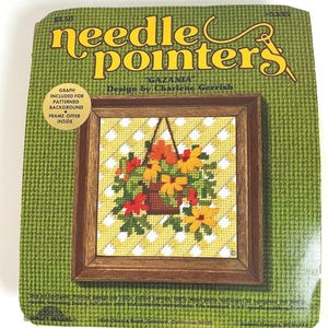 May include: A needlepoint kit titled needle pointers Gazania by Charlene Gerrish. The packaging features a green houndstooth background and a central image of a finished needlepoint of orange and yellow flowers in a hanging basket.