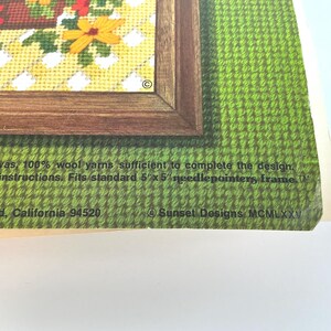 May include: A needlepoint kit package featuring a floral design in a brown frame, with text stating: cotton canvas, 100% wool yarns sufficient to complete the design, complete instructions. Fits standard 5" x 5" needlepointers frame. Sunset Designs MCMLXXV.