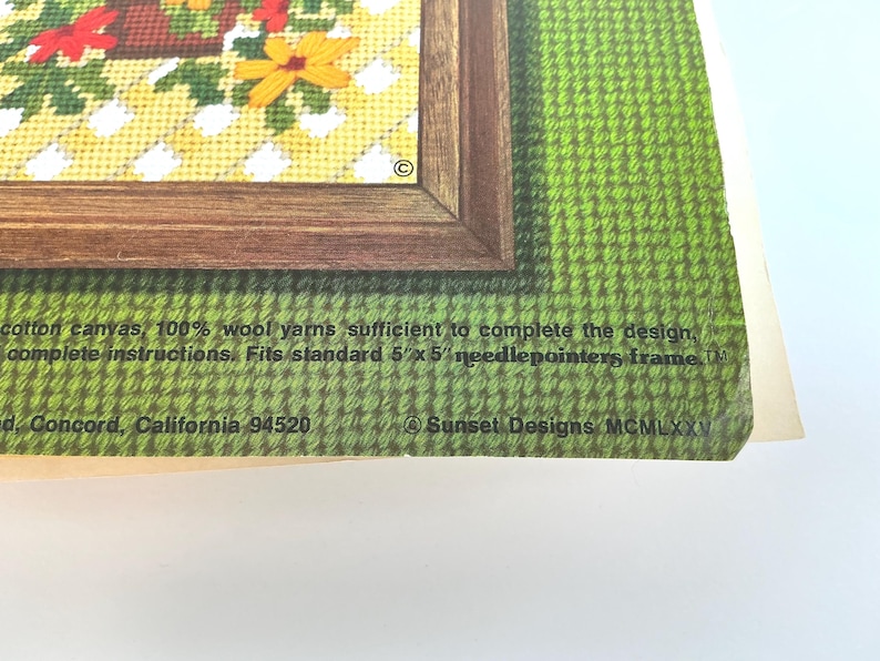 May include: A needlepoint kit package featuring a floral design in a brown frame, with text stating: cotton canvas, 100% wool yarns sufficient to complete the design, complete instructions. Fits standard 5" x 5" needlepointers frame. Sunset Designs MCMLXXV.