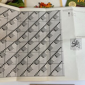 May include: A large, folded paper needlepoint pattern chart featuring a black and white grid design with repeating geometric shapes. The document includes a legend for background colours, instructional text, and small illustrations of finished floral projects.
