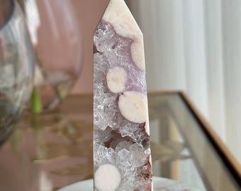 May include: A polished crystal tower featuring a pointed top, characterized by a combination of translucent clear quartz sections and opaque, rounded cream-colored inclusions set within a pale lavender and white mineral matrix.