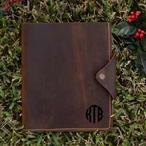 May include: A brown leather journal with a flap closure and a monogrammed circle with the initials "KTB" on the front.