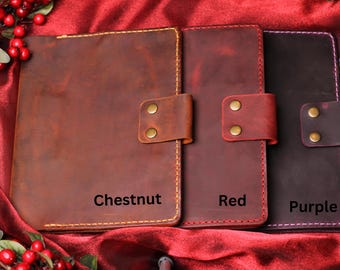 May include: Three leather journals in chestnut, red, and purple. Each journal has a flap closure with brass-colored rivets and stitched edges. The chestnut journal is labeled "Chestnut", the red journal is labeled "Red", and the purple journal is labeled "Purple".
